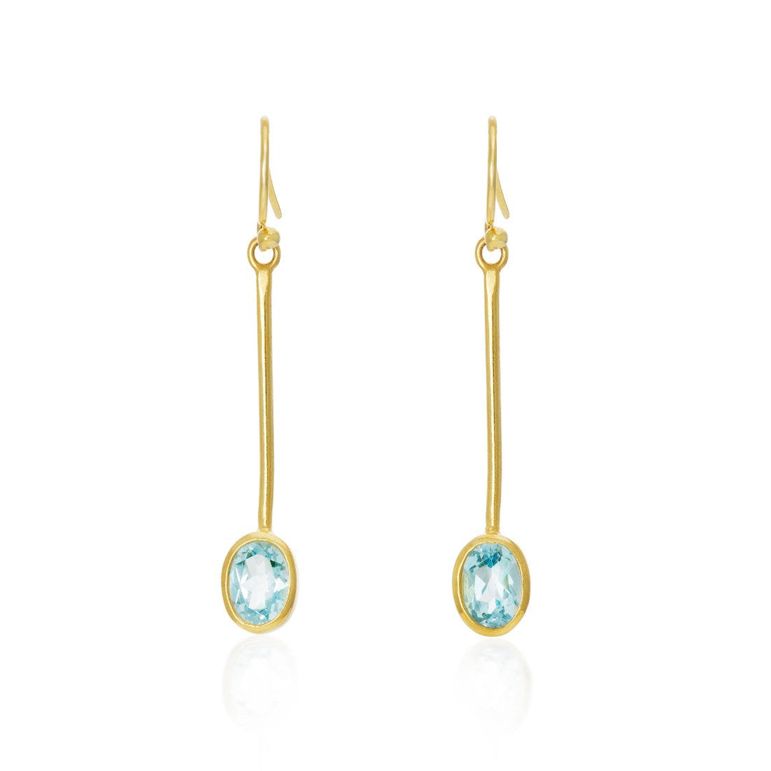 The Sequola Earrings in various gemstones by Gallardo & Blaine Designs are minimalist gold drop earrings featuring thin, elongated bars that hang vertically, each ending with an oval-cut, pale blue gemstone. These sleek and elegant dangle earrings have a simple hook closure at the top, highlighting the delicate stones.