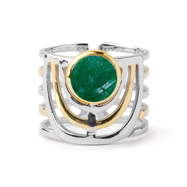 A bold jewellery design, the Solar Ring in various gemstones by Gallardo & Blaine Designs features an open band with a round, green gemstone in the center, surrounded by a gold bezel setting. The band splits into multiple parallel sections, creating an intricate and modern look.