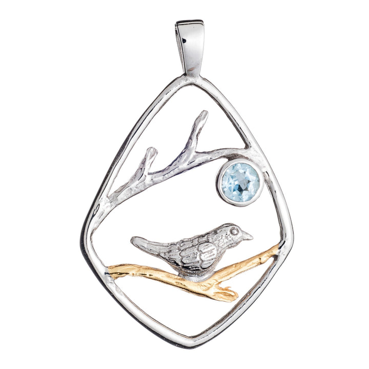 The Gallardo & Blaine Designs Song Bird Pendant features a mixed metal design of a song bird perched on a branch. The bird and branch are encased in a diamond-shaped sterling silver frame. A light blue gemstone adds a touch of color above the bird. The pendant has a sleek loop for attaching to a chain.