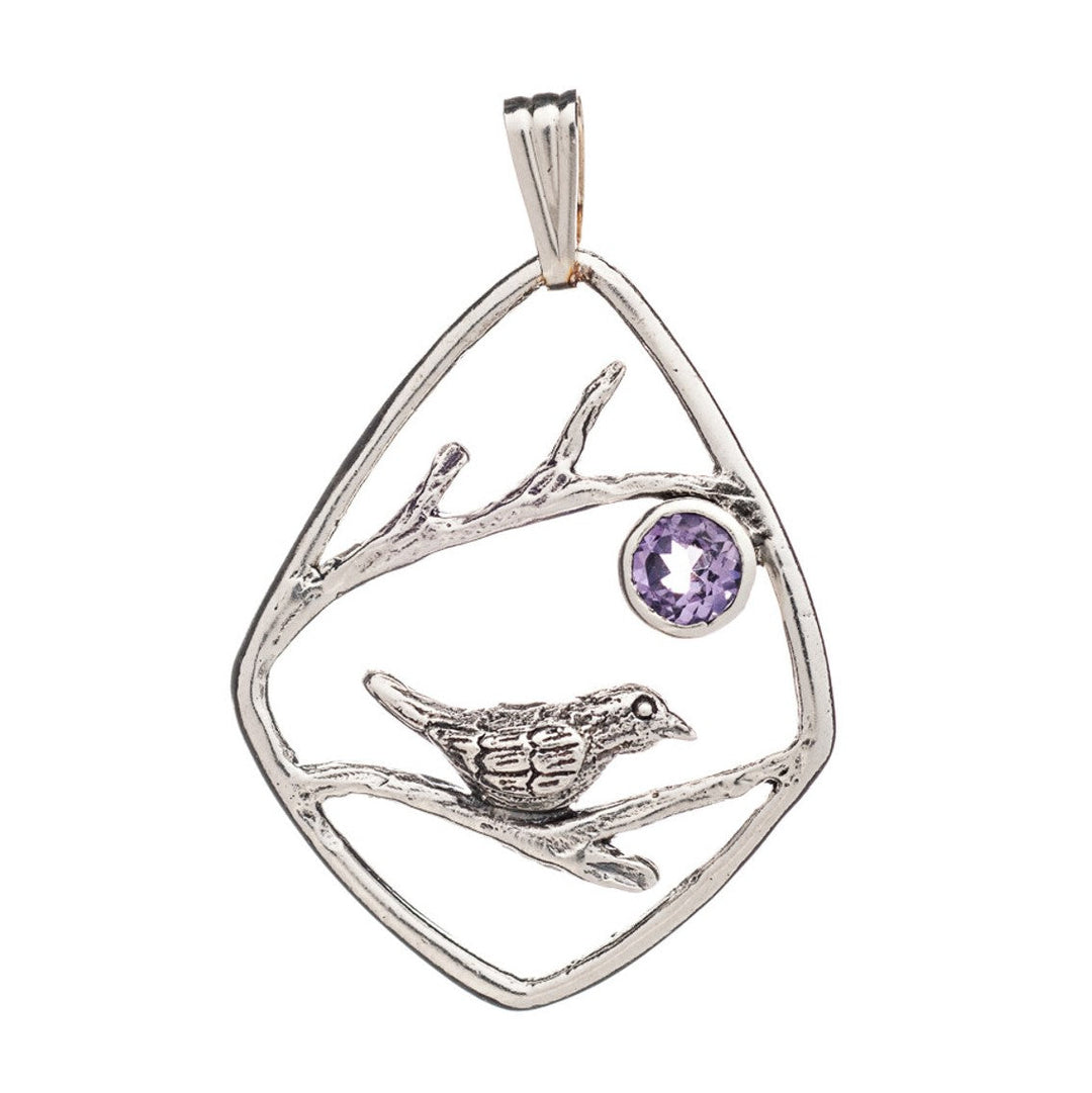 A romantic pendant crafted in sterling silver features an open-frame diamond shape with a song bird perched on a branch in the center. The Song Bird Pendant by Gallardo & Blaine Designs has an amethyst gemstone set inside next to the bird, adding a touch of elegance.