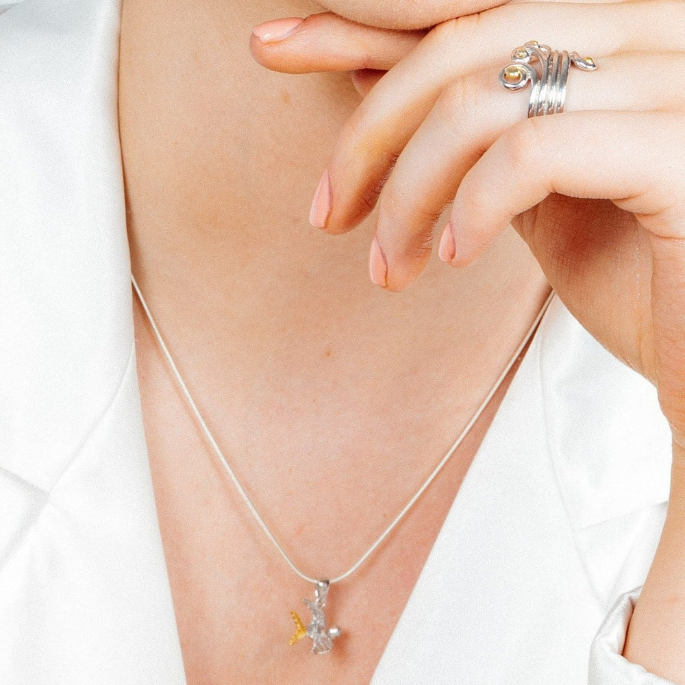 Close-up of a person wearing a sterling silver snake chain necklace with a small Wildlife Pendant - Swallow With Chain by Gallardo & Blaine Designs and a silver ring featuring an orange stone on their index finger. The person is touching their lips with the adorned finger, dressed in a white garment.