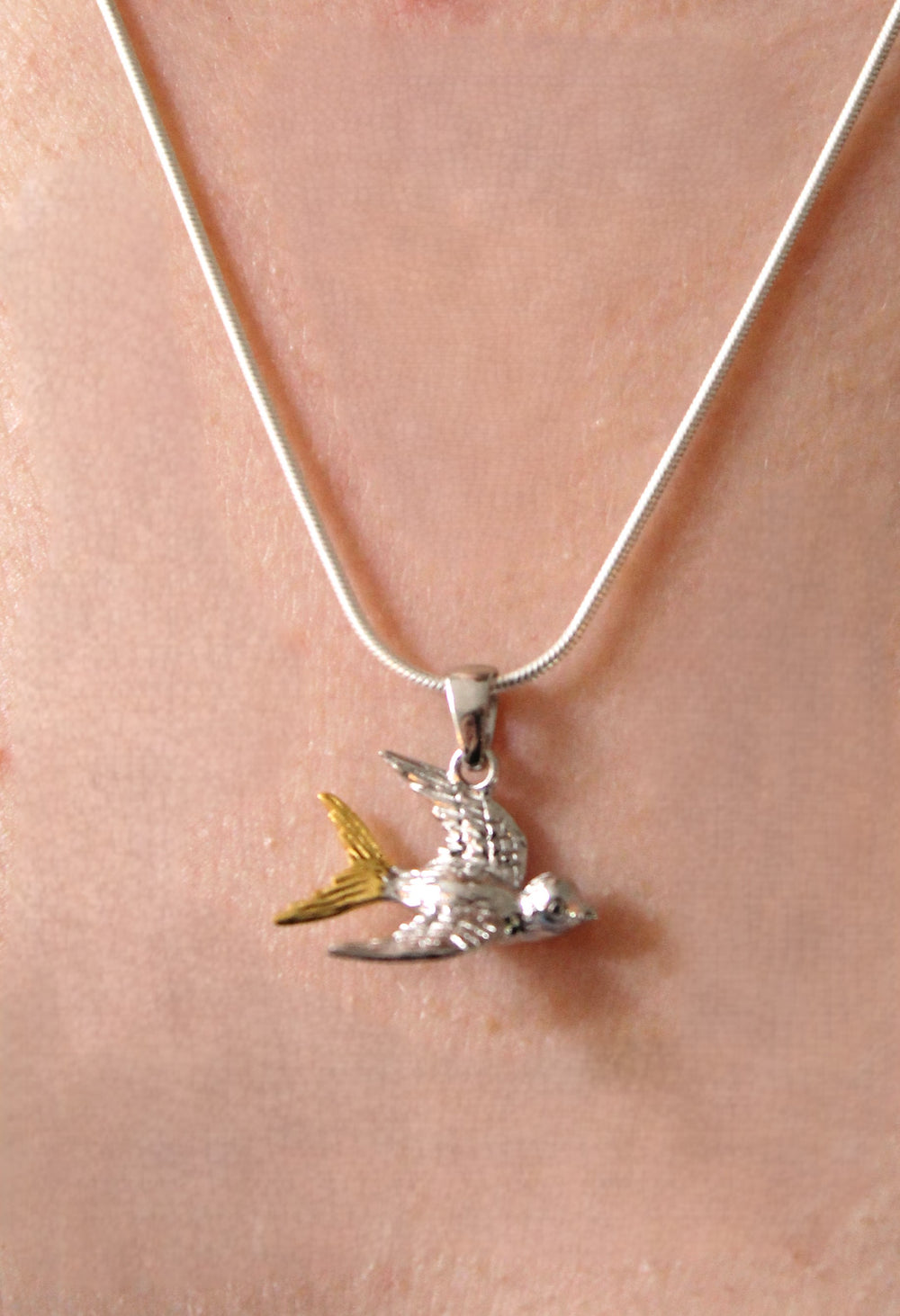 Gallardo & Blaine Designs’ Wildlife Pendant – Swallow With Chain features a sterling silver swallow in flight with yellow tail accents, worn around the neck.