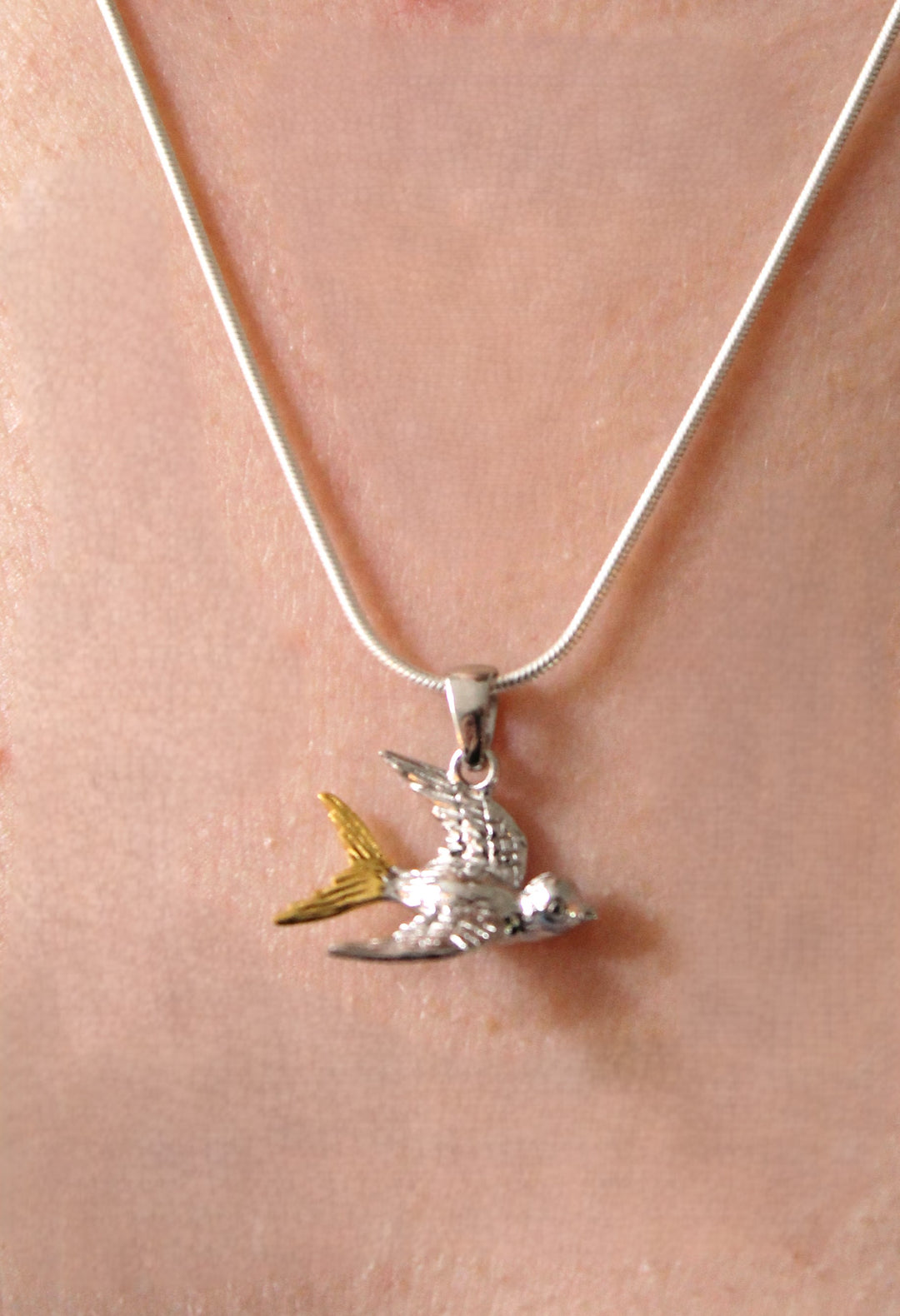 Gallardo & Blaine Designs’ Wildlife Pendant – Swallow With Chain features a sterling silver swallow in flight with yellow tail accents, worn around the neck.