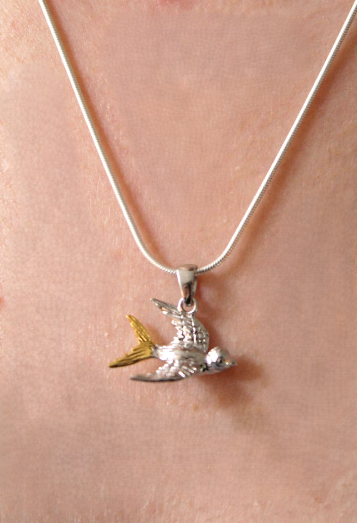 Gallardo & Blaine Designs’ Wildlife Pendant – Swallow With Chain features a sterling silver swallow in flight with yellow tail accents, worn around the neck.