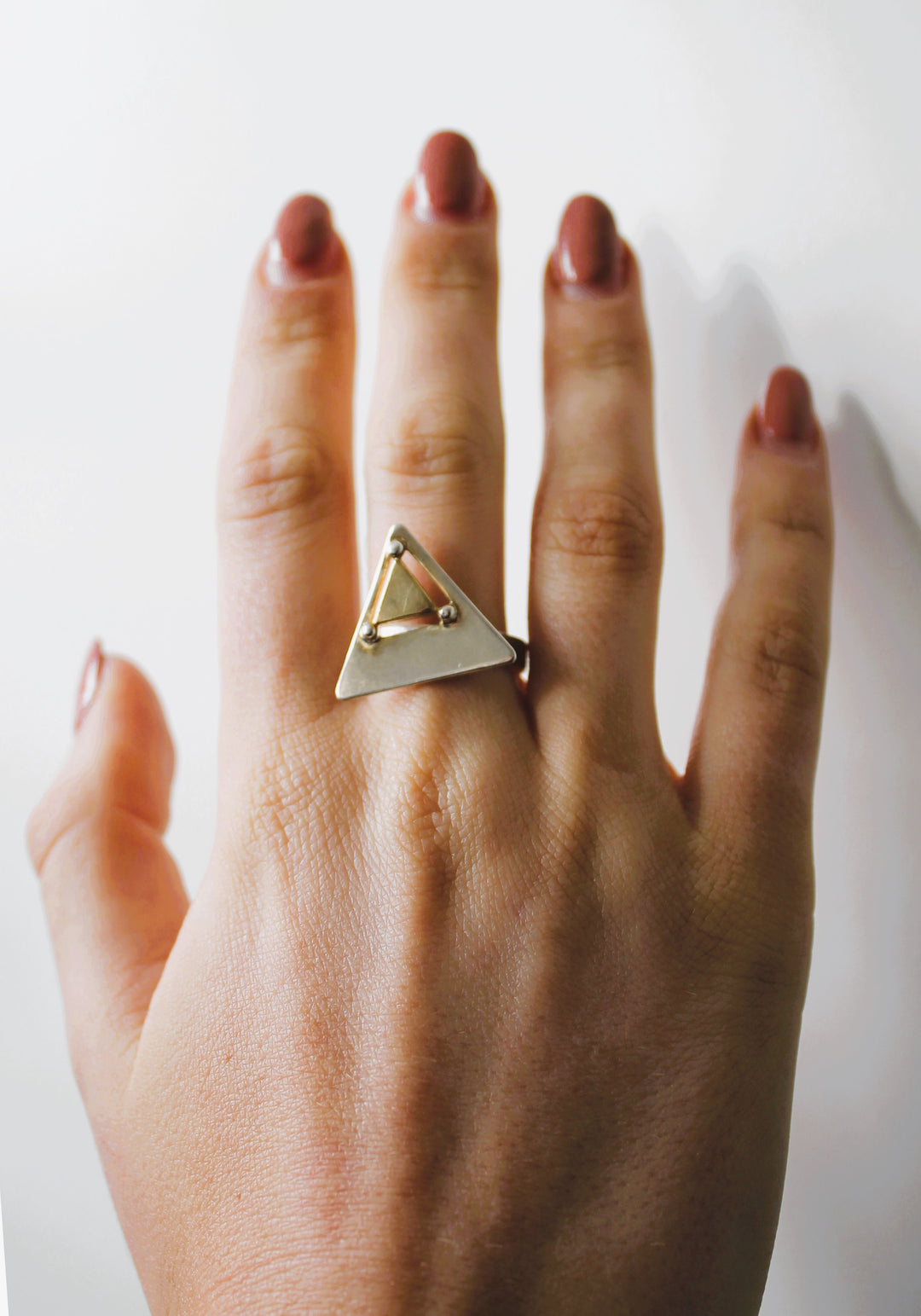 A hand with neatly manicured nails wears the Triune Ring by Gallardo & Blaine Designs—a sterling silver ring featuring a geometric triangle design—on the middle finger, set against a plain white background.