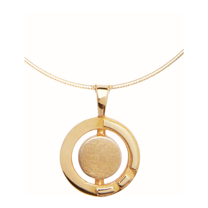 A gold vermeil necklace featuring a circular pendant. The pendant has a solid central circle enclosed within an open circular frame with a small rectangular cutout in the bottom right quadrant. Inspired by Irish heritage jewelry, the Urú Large Pendant & Chain by Gallardo & Blaine Designs features a simple gold snake chain.