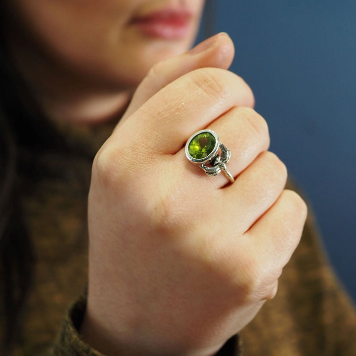 A close-up of a person's hand showing a delicate and dainty silver Daydream Ring in various gemstones by Gallardo & Blaine Designs. The person's face and background appear out of focus, adding to the allure of this timeless piece. The person is wearing a brown textured fabric.