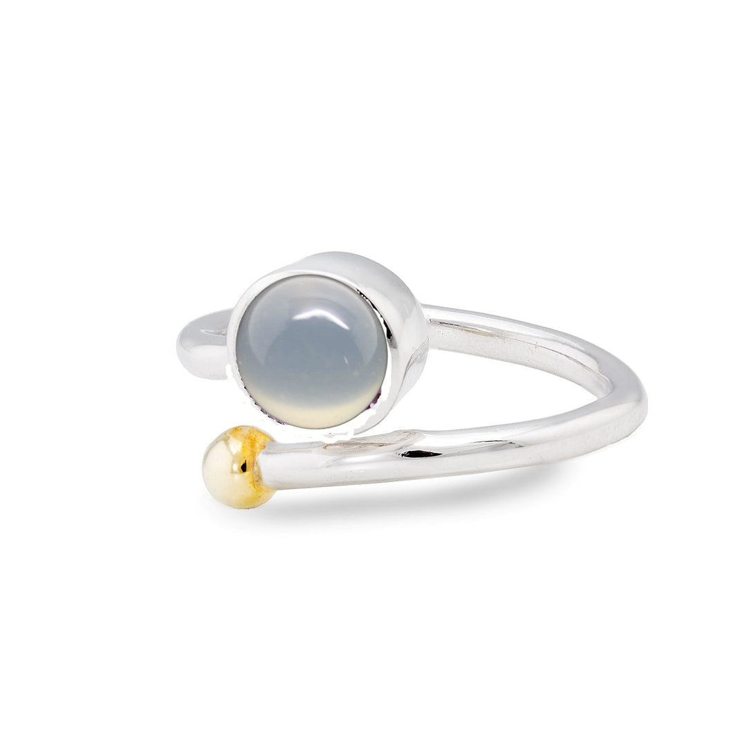 A silver and gold jewelry piece, the Honeysuckle Ring in Silver Gold & gemstones by Gallardo & Blaine Designs highlights a round, translucent white gemstone on one end and a small gold bead on the other. The open band design exudes modern minimalism.