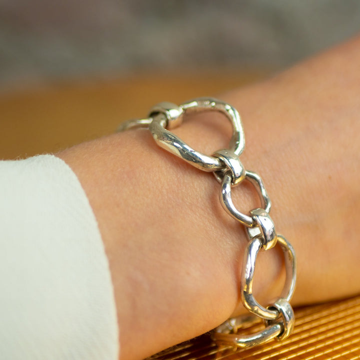 A close-up of a person wearing a Sea Honey Bracelet Silver by Gallardo & Blaine Designs with thick silver links. The person is dressed in a light-colored long sleeve top, and the background is blurred.