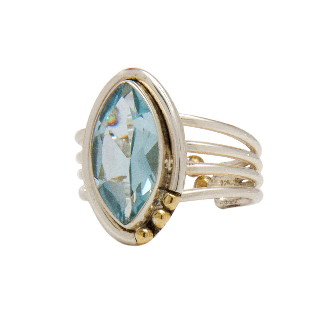 A silver Art Deco adjustable ring, the Tulip Ring in various gemstones by Gallardo & Blaine Designs, featuring a large marquise-cut blue gemstone at its center. The band consists of multiple thin loops that combine together near the base of the stone, accented with small gold embellishments on one side.