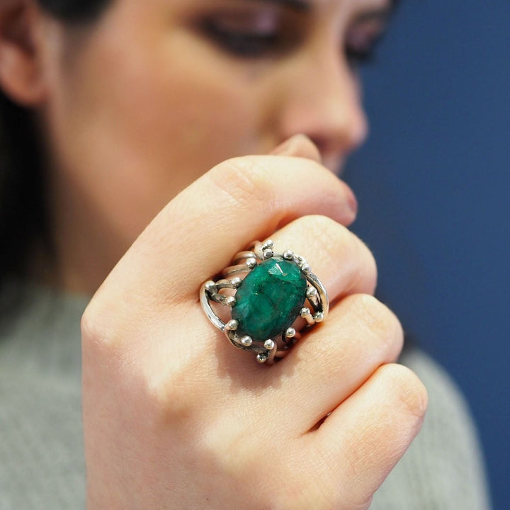 Close-up of a person's hand wearing a chunky statement gemstone ring with an elaborate silver setting. The person's face is blurred in the background, focusing attention on the Willow Ring in various gemstones by Gallardo & Blaine Designs.