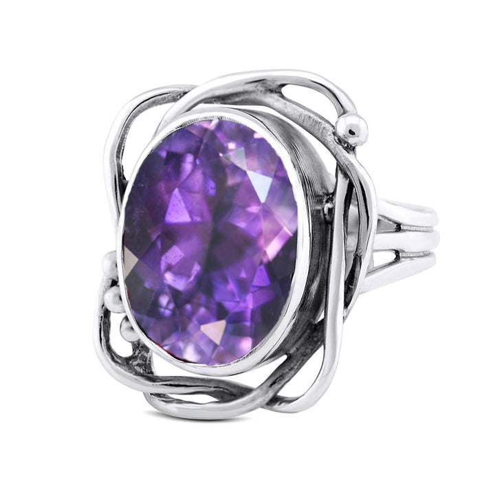 An Arthurian silver ring featuring an ornate design with an intricate, swirled band. The centerpiece is a large, faceted purple gemstone, possibly an amethyst, set in an elegant and artistic setting. This vintage, handcrafted Whirlpool Ring in various gemstones by Gallardo & Blaine Designs exudes timeless charm and sophistication.