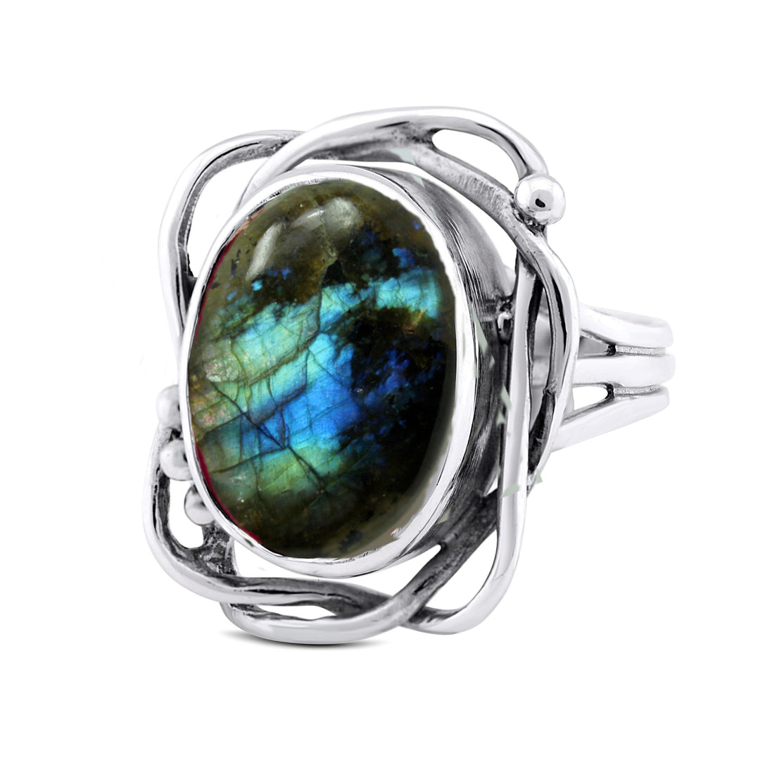 An adjustable silver ring with an oval labradorite gemstone. The gemstone showcases vibrant blue, green, and hints of yellow iridescence. The intricate silver setting features artistic swirls and loops around the gemstone, making this a stunning Whirlpool Ring in various gemstones by Gallardo & Blaine Designs.