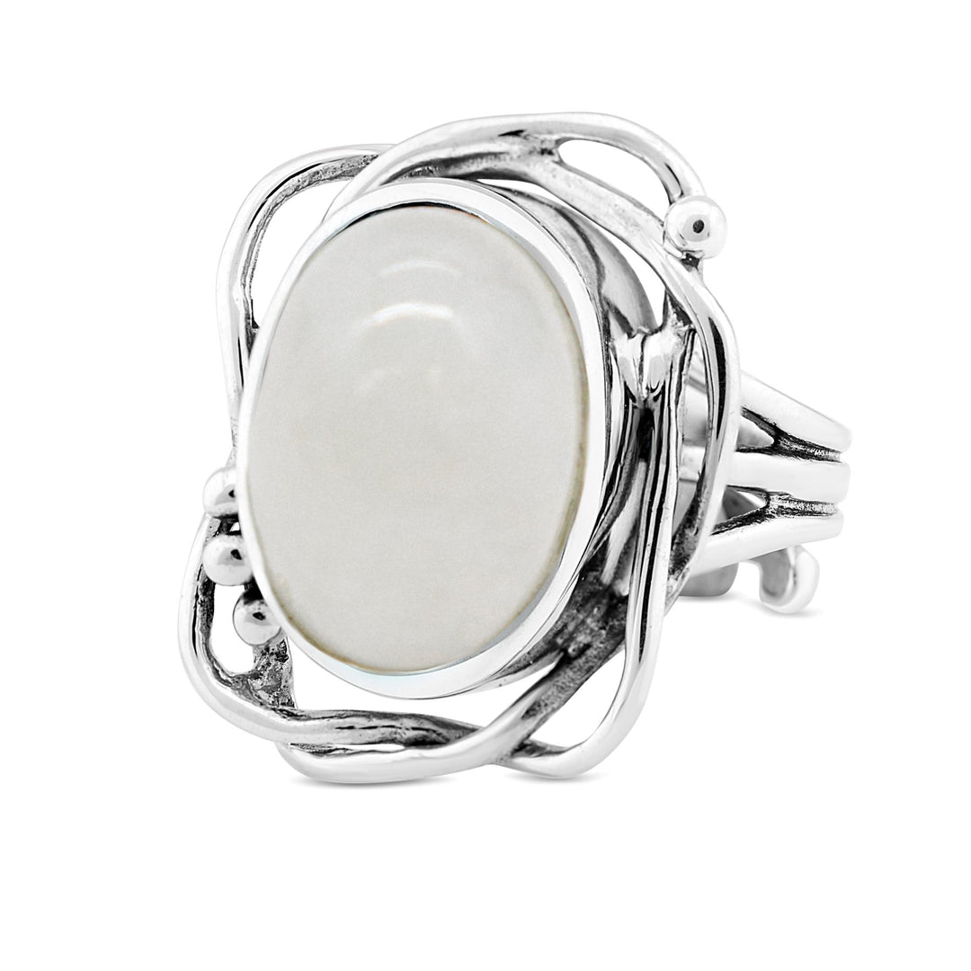 A silver ring with an intricate, vine-like design encircles an oval-shaped, smooth white gemstone. The band is split into several strands that intertwine around the central stone, creating an elegant and organic appearance reminiscent of a timeless Arthurian Whirlpool Ring in various gemstones by Gallardo & Blaine Designs.