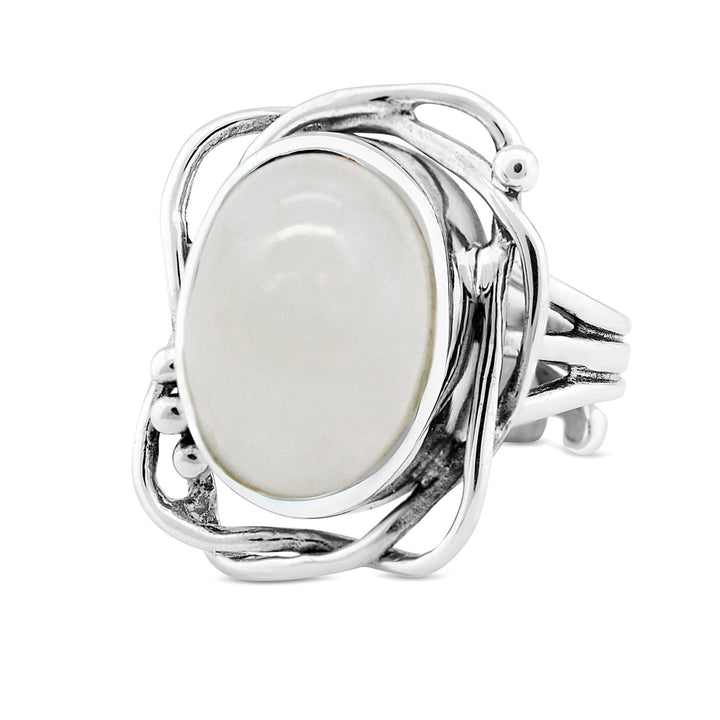 A silver ring with an intricate, vine-like design encircles an oval-shaped, smooth white gemstone. The band is split into several strands that intertwine around the central stone, creating an elegant and organic appearance reminiscent of a timeless Arthurian Whirlpool Ring in various gemstones by Gallardo & Blaine Designs.