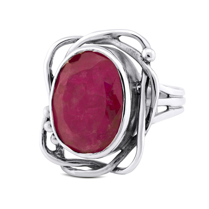 This Gallardo & Blaine Designs Whirlpool Ring in various gemstones features an oval-shaped, faceted ruby gemstone in the center. The ruby is encased in an intricate, openwork silver setting with swirling patterns, creating an elegant and artistic design. The band splits into multiple sections leading up to the setting.