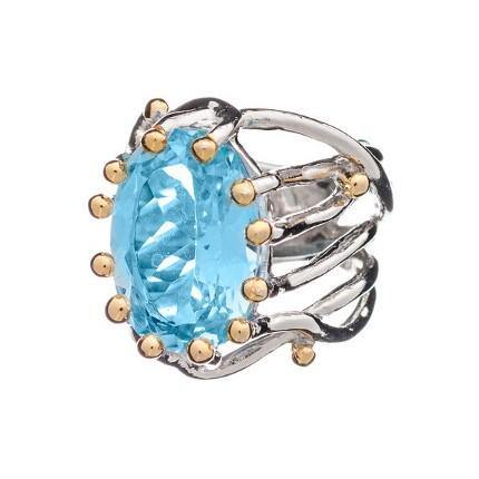 The Willow Ring in various gemstones by Gallardo & Blaine Designs features a large, faceted oval blue gemstone at its center, held by multiple gold prongs on an intricate silver band. This modern and elegant adjustable ring is perfect as a chunky statement gemstone ring for any occasion.