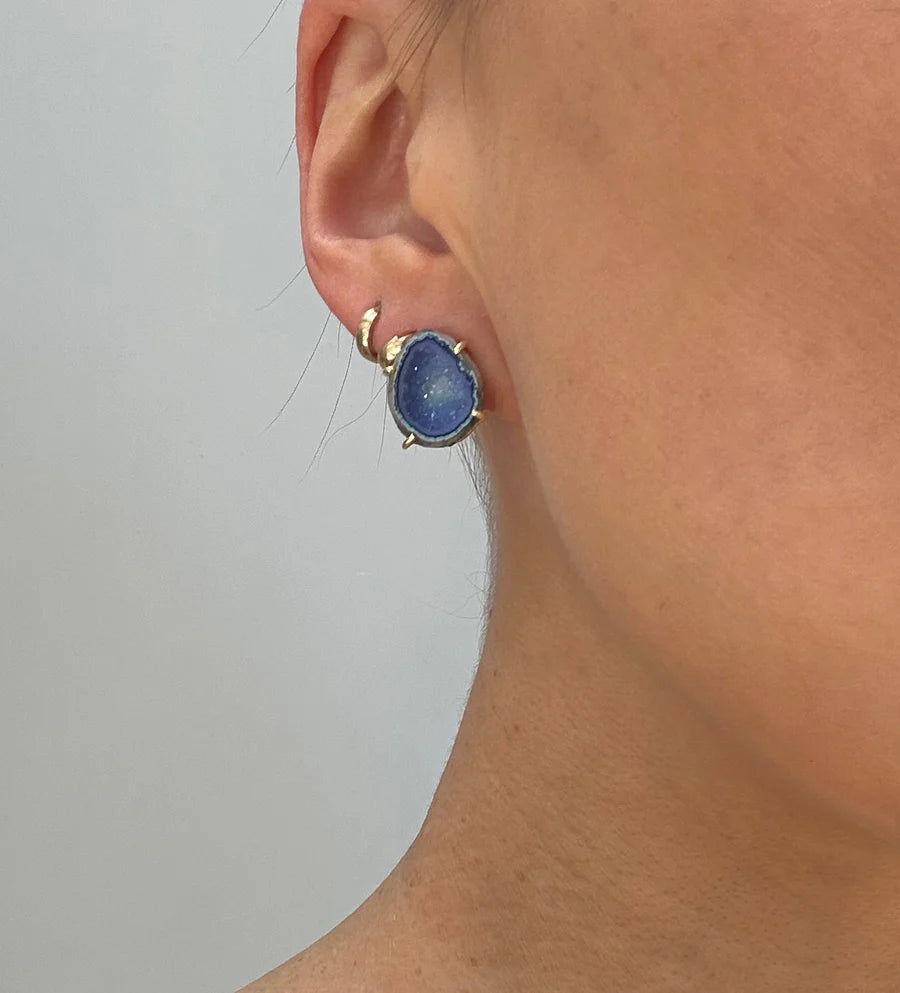 Close-up of a person's ear wearing Aria V Geode Tassel Earrings—round aqua blue geodes in gold prong settings, with an extra small hoop above; smooth skin and a plain light grey background. Handmade in Dublin.