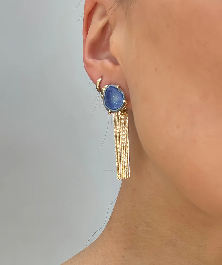 Close-up of a woman's ear wearing Aria V Geode Tassel Earrings in aqua blue with gold chains, set against a neutral background. These handmade earrings from Dublin bring unique elegance and color to any style.