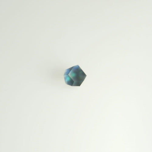 A single Fruit Bijoux Ring Top Ghost with a dark, iridescent surface lies against a plain white background. Accentuated with sterling silver edges, the Fruit Bijoux product appears to have a prismatic quality, reflecting hues of blue and green.