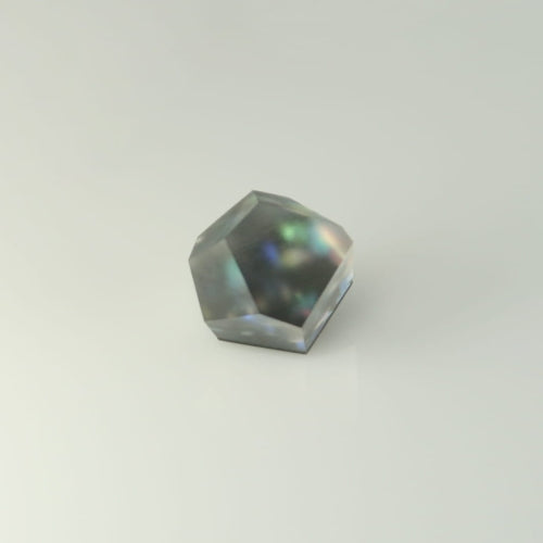 A geometric, gray gemstone with an irregular faceted shape, displaying subtle rainbow reflections under light, rests on a smooth, gradient background atop a Fruit Bijoux Fruit Bijoux Ring Top Ghost.