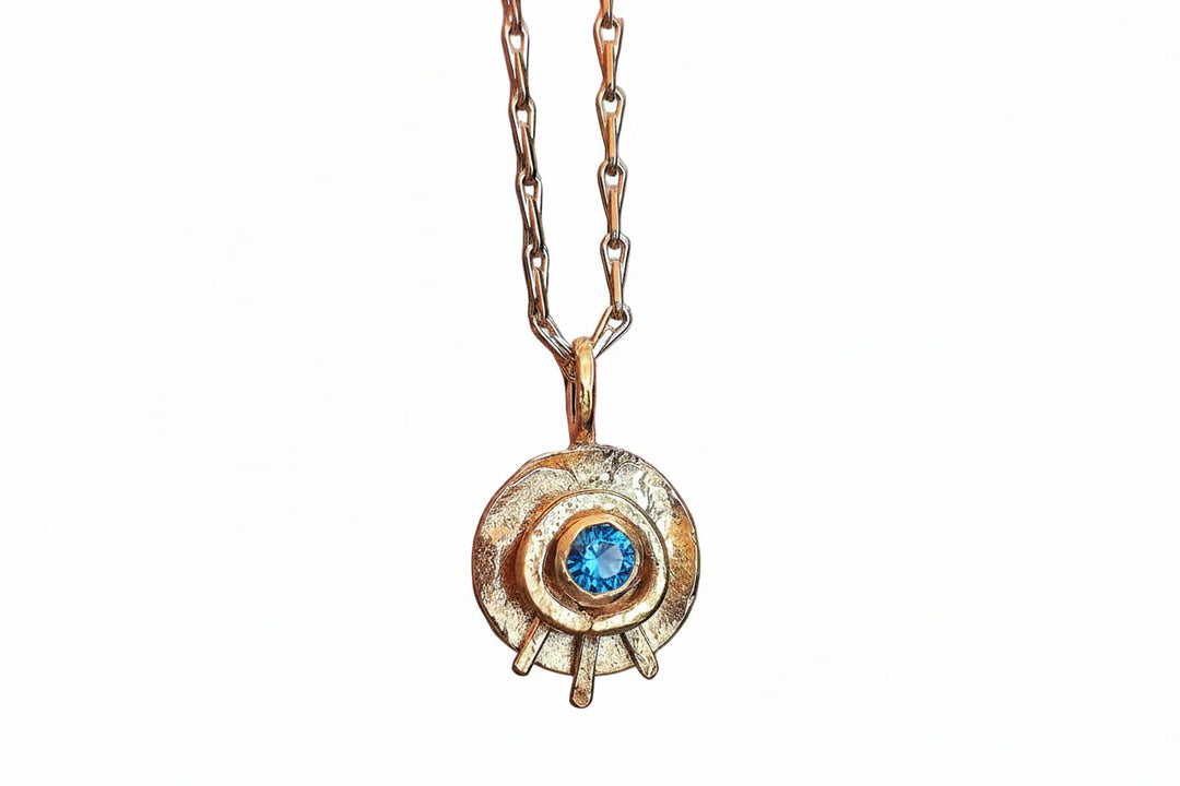 The Caroline Stokesberry-lee Celestial Eye Pendant Gold in Blue Topaz is a gold plated sterling silver necklace with a bright blue topaz center, displayed on a gold chain against a plain white background.