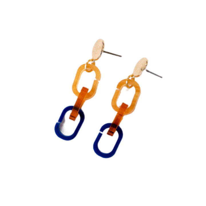 A pair of lightweight dangle earrings with stainless steel posts. Each earring features three interlocking chain links: the top two links are a translucent amber color, and the bottom link is royal blue, creating a modern and bold design. Handmade in Belgium for an exquisite touch. Introducing the Gold, Orange & Navy Fire Acrylic Earrings from Studio Nok Nok.