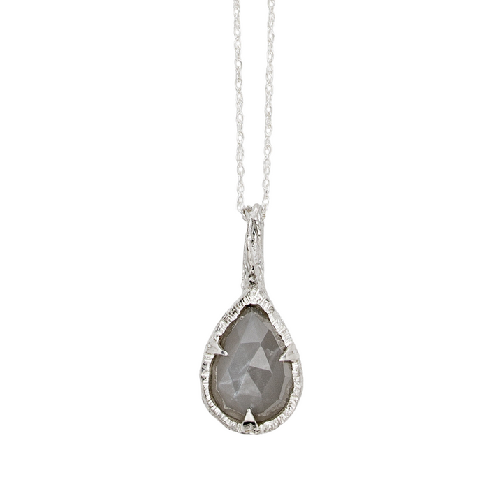 A delicate sterling silver necklace, the Thorn Teardrop Pendant by Abbie Dixon, features a teardrop-shaped thorn pendant with a faceted gray moonstone. The pendant has an intricate textured setting, hanging on a fine silver chain. The gemstone has a translucent, slightly marbled appearance.