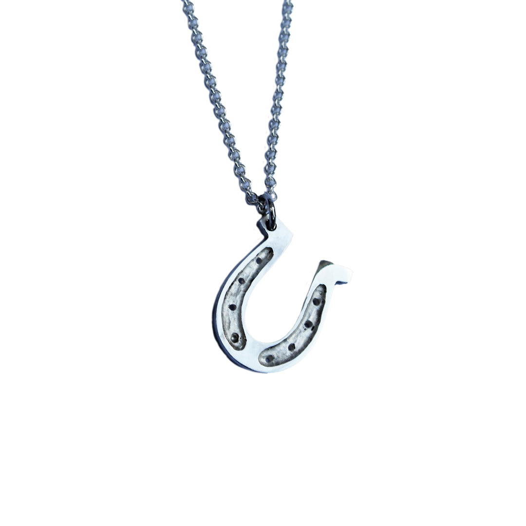 The Kate Murphy Horseshoe Silver Pendant features a sterling silver horseshoe charm with decorative indents, hanging on a fine chain and symbolizing good luck.