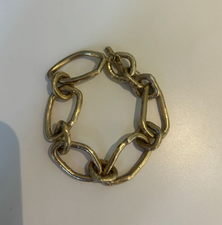 The Cinder Bracelet by Madeleine Blaine, featuring large, irregular oval links in a chunky gold chain design, is displayed on a plain white surface.