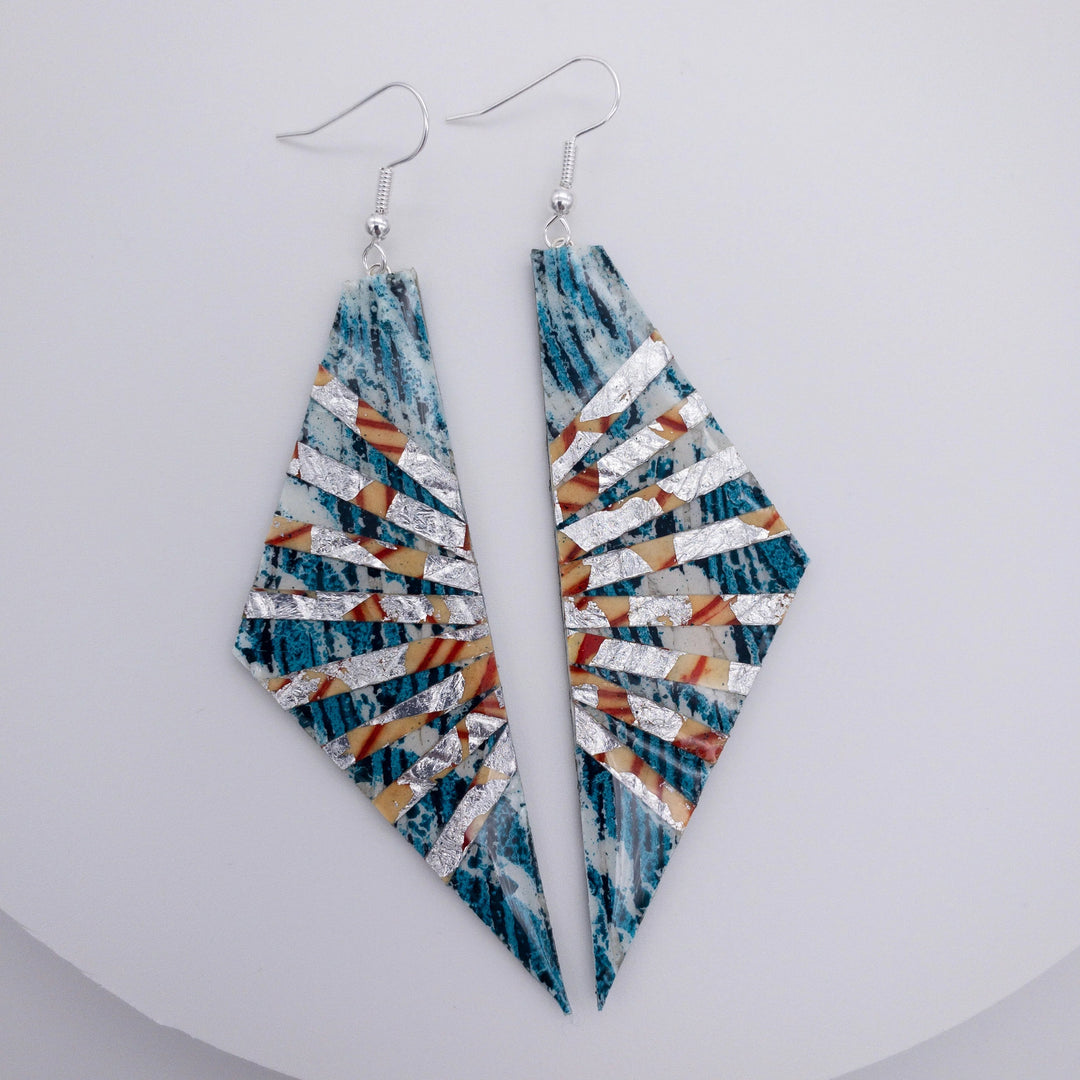 A pair of Adabel Batik Textile Earrings in Teal/Silver/Orange by Rothlú featuring an abstract design. The earrings, made from sterling silver, showcase alternating stripes in blue, orange, and green with a striking diamond-like shape and a hook for wearing. Super-lightweight and placed against a plain white background.