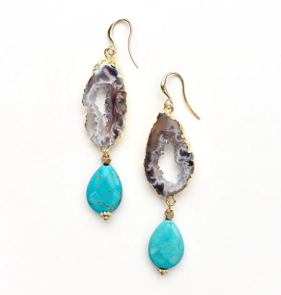 A pair of Cameo Earrings by Aria V featuring raw geode slices in white and purple hues, adorned with turquoise teardrops at the bottom. The earrings are set in gold and have hook fastenings.