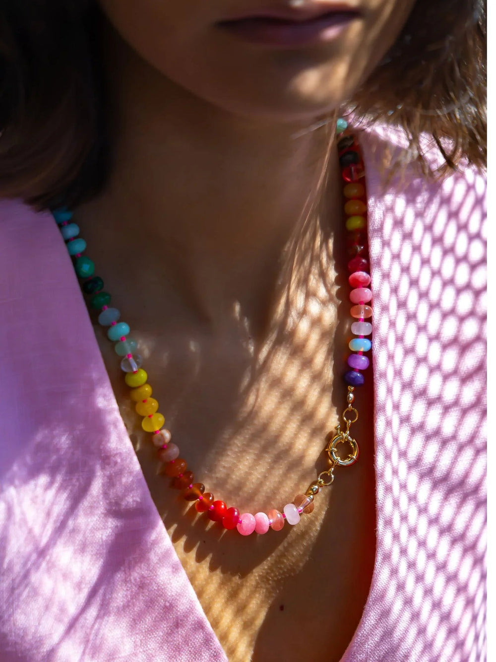 Close-up of a colorful beaded necklace worn by a person with a pink garment.