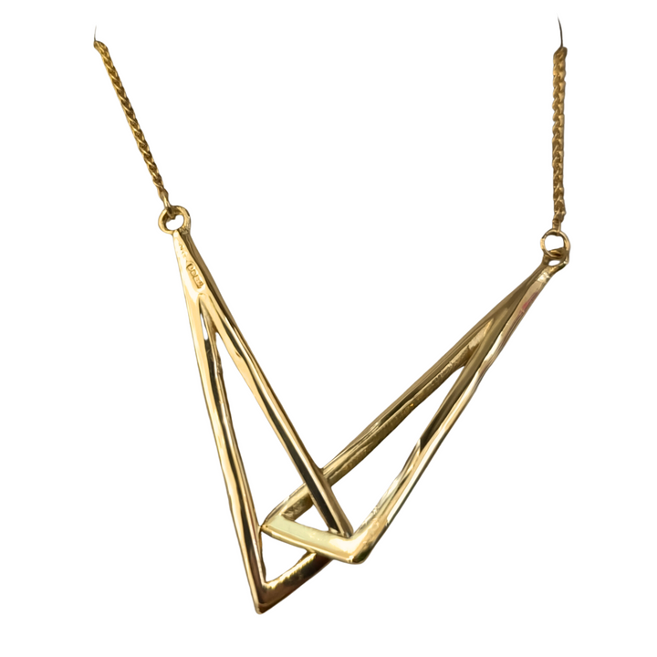 The Miriam Wade Le Cheile Pendant Large 9ct Yellow Gold features an abstract geometric pendant. The linked pendant consists of two interlocking triangular shapes with sharp, clean lines, suspended on a thin 9ct yellow gold chain. The design is modern and minimalist, offering an elegant and contemporary look, secured with a handmade T-bar catch.