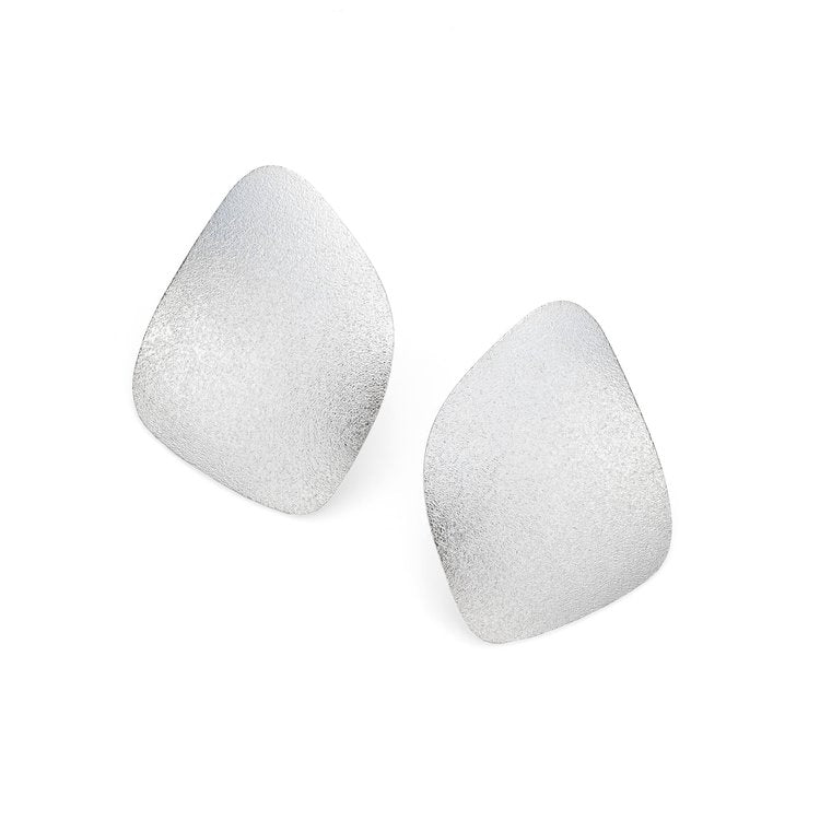 A pair of asymmetrical, sterling silver earrings with a textured surface. Each earring features a smooth, irregular shape, providing a modern and minimalist aesthetic. The earrings have a frosted finish, highlighting their elegant design. These are the Freeform Wing Studs Silver by Leoma Drew.