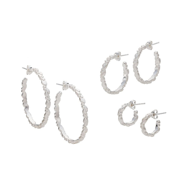 A set of three pairs of Leoma Drew Freeform Layered Wing Hoop Earrings in Frosted Silver, each with a textured surface. The set includes large, medium, and small hoop sizes in Freeform Layered Wing designs, displayed against a white background. The earrings are designed with post and butterfly back closures.