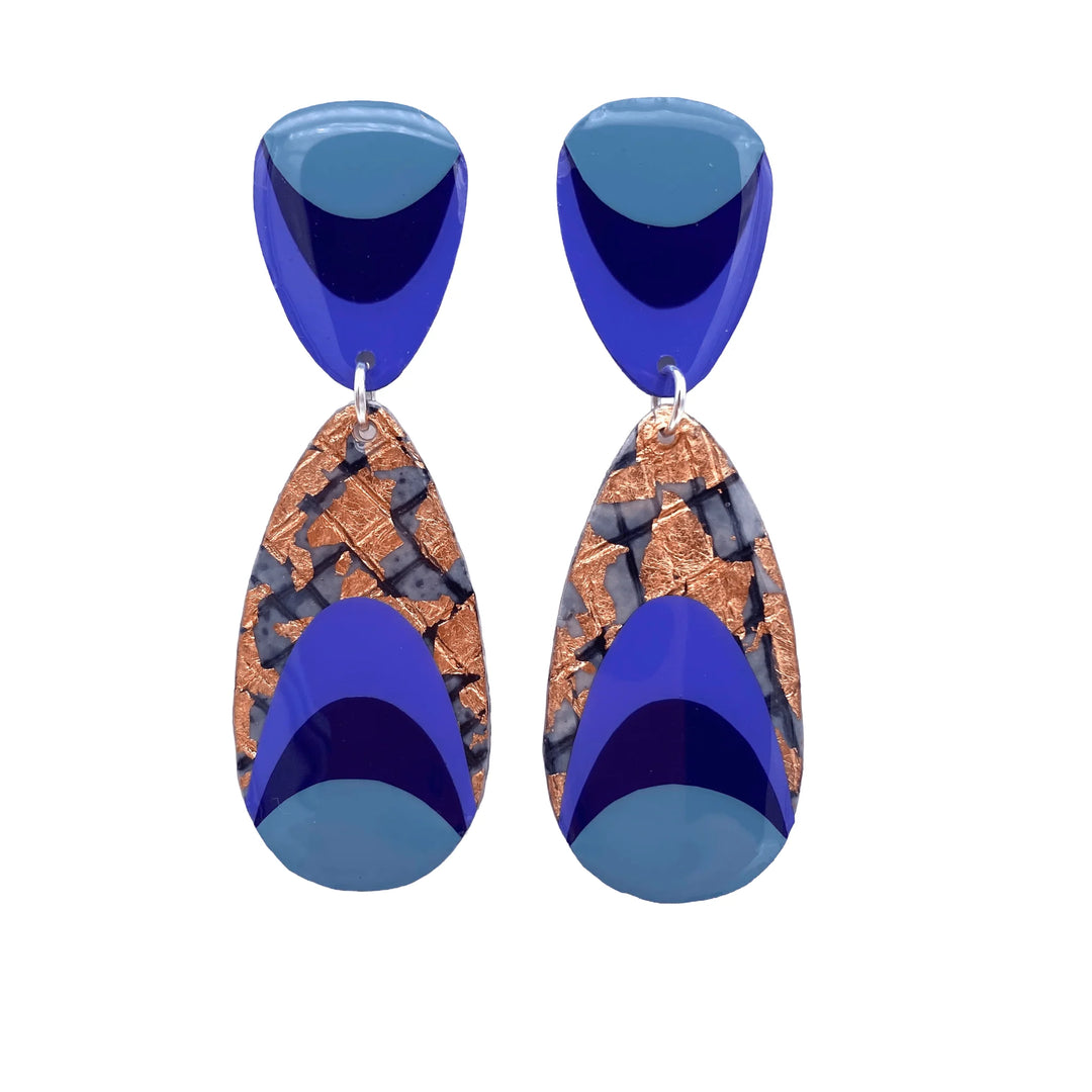 Rothlú’s M’anam Batik Textile Earrings feature hypoallergenic dangle design in silver, with geometric shapes, cornflower blue and sapphire sections, plus rose-gold and black mosaic-like textured accents.