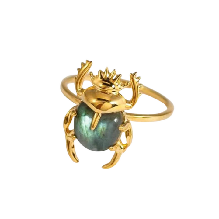 A Marie June Jewellery Sacred Scarab Gemstone Ring crafted in 24k gold vermeil, featuring a beetle with an iridescent green labradorite stone as its body. The beetle's intricately detailed golden legs and antennae wrap partially around the band, creating an exquisite piece of natural hand-carved artistry.