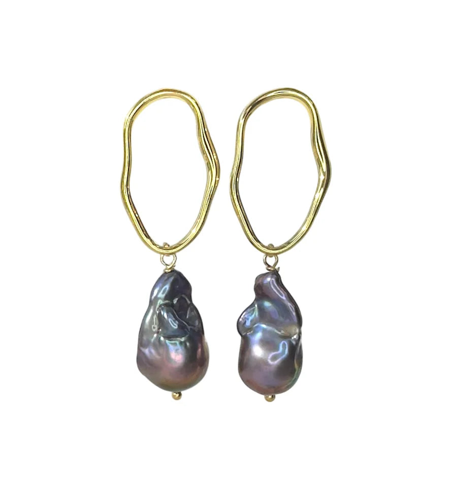 The Millie Earrings by Aria V feature irregular oval gold electroplated brass hoops, each accented with a uniquely shaped iridescent baroque pearl. Available in various colours.