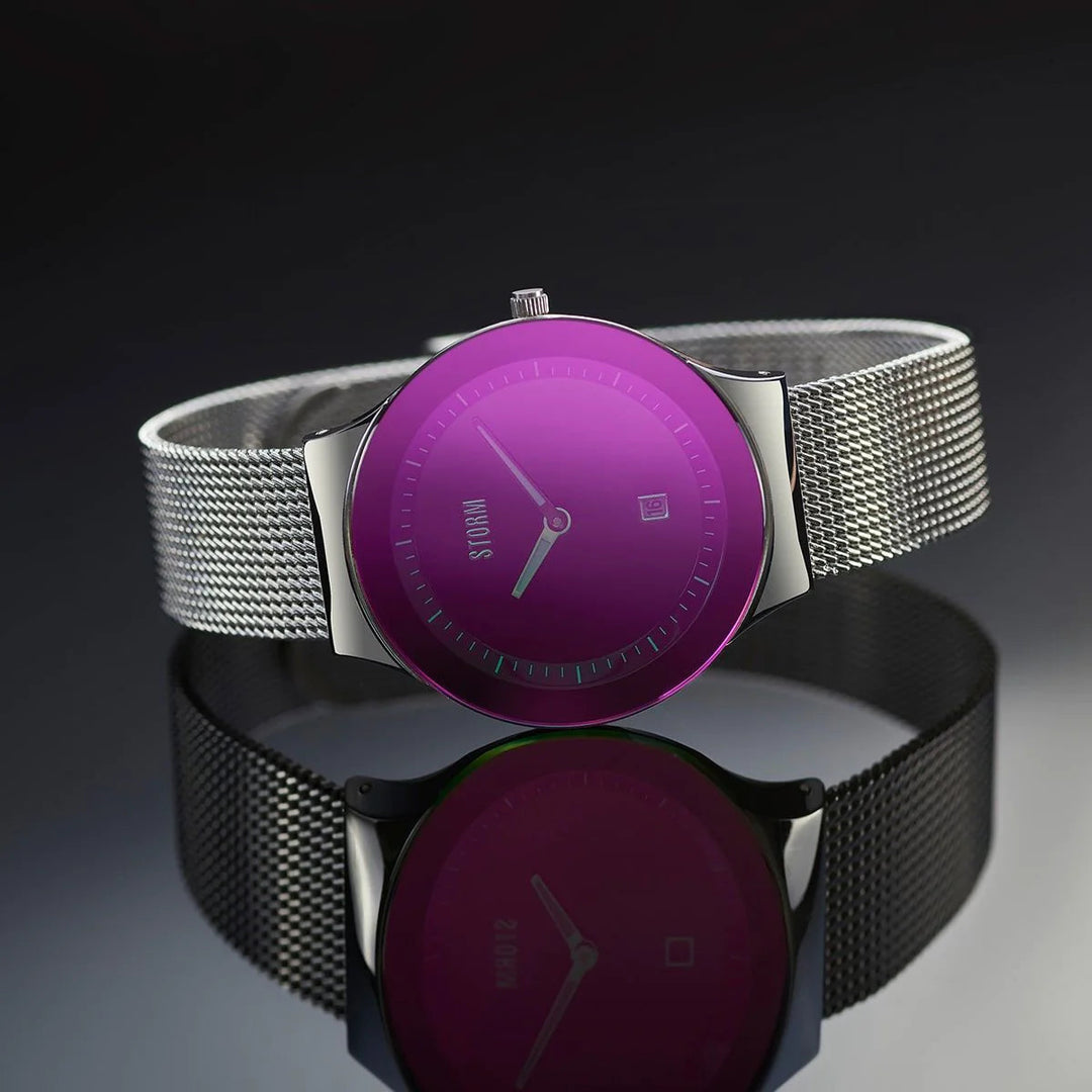 A Storm Mini Sotec Lazer Purple watch with a vibrant purple dial, showing gold-plated stainless steel hour, minute, and second hands. The watch features a silver mesh strap, and the text "Storm Watches" is visible on the dial. Placed on a reflective black surface, it creates a mesmerizing mirrored effect.