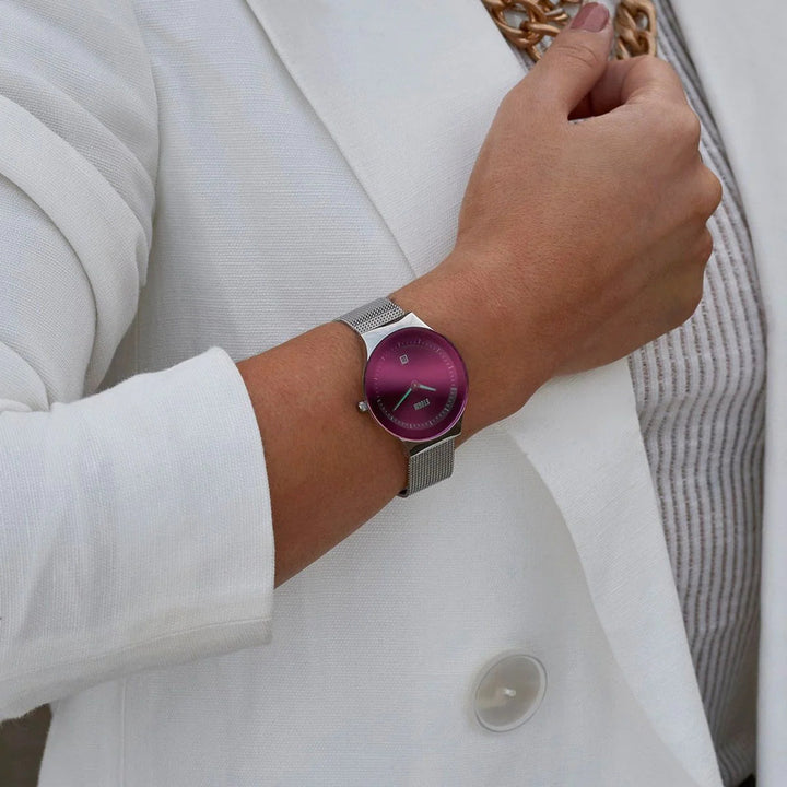 A person wearing a white blazer and a light striped shirt is displaying a stylish Storm Watches Storm Mini Sotec Lazer Purple watch with a vibrant purple face and a silver mesh band. The person's hand is partially visible, showing neatly manicured nails with light polish.