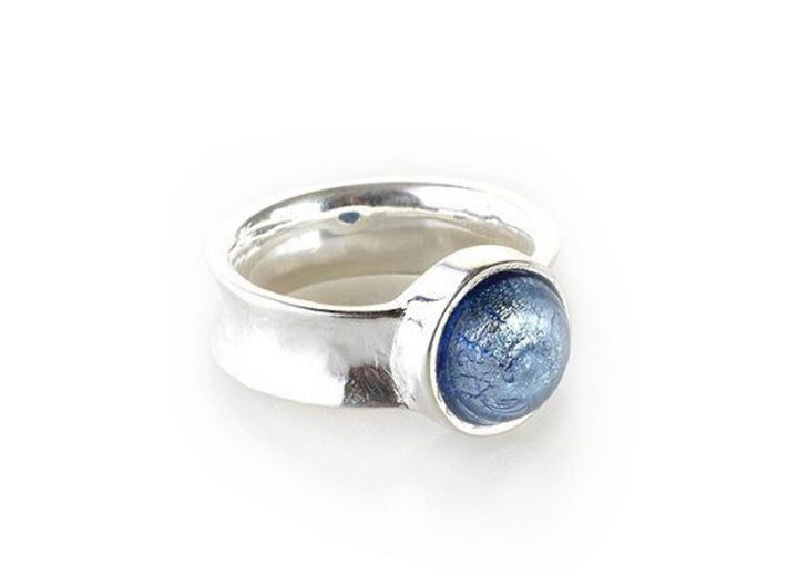 The Murano Half Perle Silver Ring 10mm by Detlef Menard is a handcrafted sterling silver ring with a wide band featuring a round, glossy, blue-tinted gemstone set in a bezel. The gemstone, resembling Murano Glass, has a cracked, marble-like pattern adding depth and texture to its appearance. The ring boasts a polished, shiny finish.