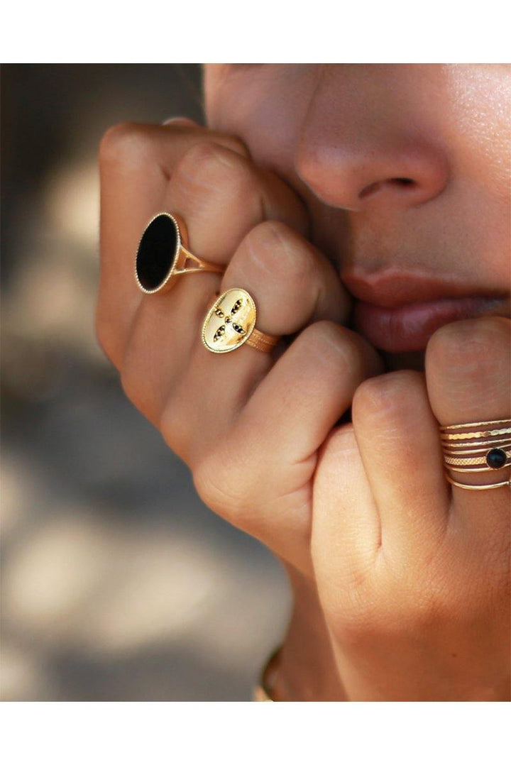 Close-up of a person resting their chin on their hands, showcasing an assortment of gold rings adorned with black natural stones, including the exquisite Frida Ring by Nilai. The background appears slightly out of focus, emphasizing the rings and the person's lips.