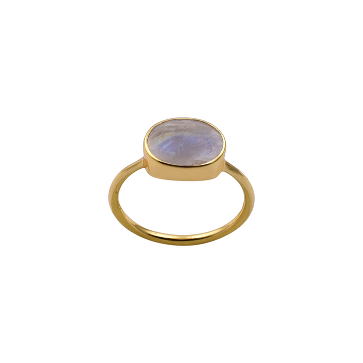 The Oval Rainbow Moonstone Gold Ring by Watermelon tropical features a round, translucent rainbow moonstone set in a simple bezel setting. The band is smooth and polished, complementing the ethereal appearance of the stone. The ring is displayed against a plain white background.