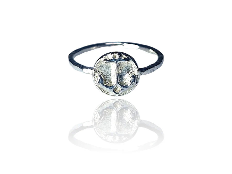 The Odyssey Ring by Pale Raven is a silver stacking ring with a round, textured abstract face, shown on a white background with a subtle reflection.