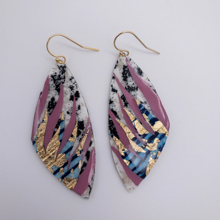 The Peitil Batik Textile Earrings in Charcoal/Deep Rose/Lapis Gold by Rothlú are one-of-a-kind, leaf-shaped earrings with an abstract design. They feature a mix of pink, black, blue, and white colors complemented by gold flake accents and gold ear hooks, all finished with a high gloss eco resin sheen.