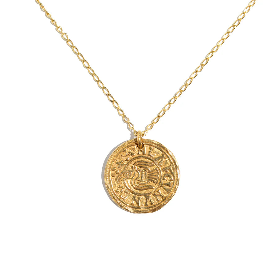The Pale Raven Penny Raven Coin Gold Plated Necklace features a delicate chain and a round, embossed Viking-inspired pendant with intricate designs, shown against a white background.