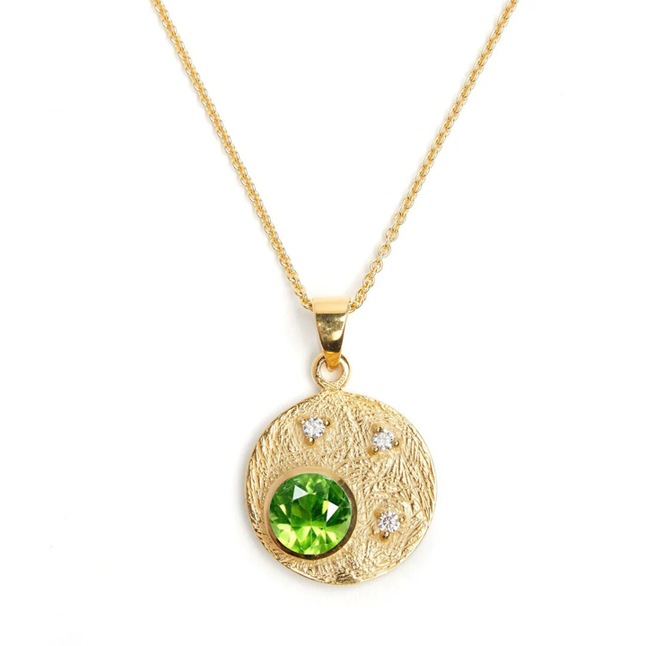 Introducing Gallardo & Blaine's Celeste Necklace: a gold masterpiece featuring a circular pendant with a large green gemstone and three sparkling cubic zirconia stones on a fine, delicate chain—an elegant addition to any jewelry collection.