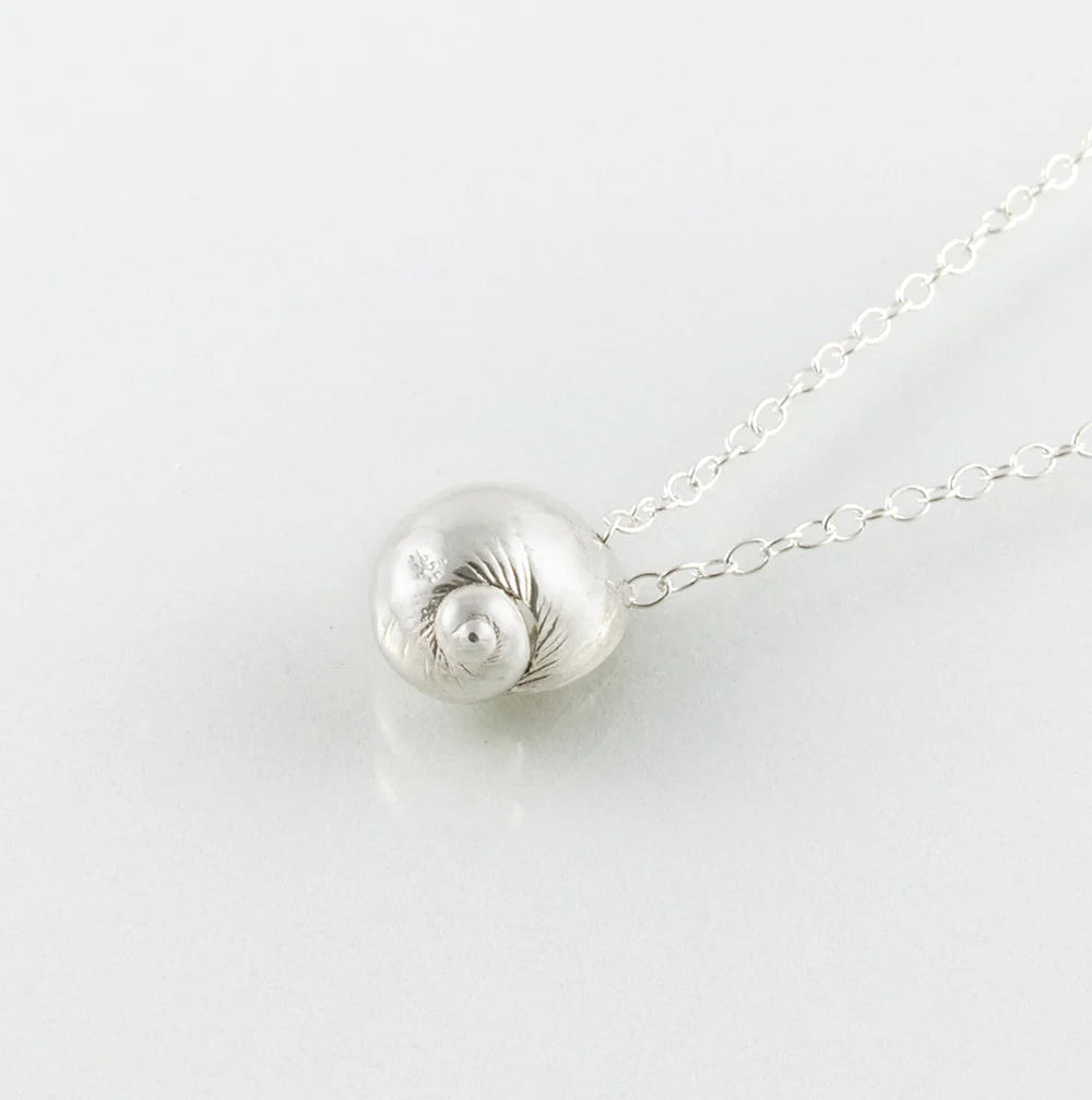 The Periwinkle Shell Necklace by Jennifer Kinnear, available in silver or gold, boasts a baby sea snail pendant intricately crafted with fine detail and suspends gracefully on a fine silver chain. The polished Mozambique shell against a plain white background enhances its undeniable charm.