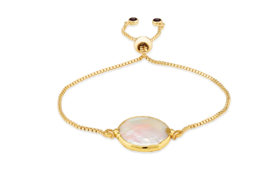 The Perle Bracelet by Aria V is a delicate gold-plated brass chain bracelet with an adjustable fastening, featuring a polished oval-shaped mother-of-pearl centerpiece set in a gold bezel. The chain ends are adorned with small, round, dark-colored beads.